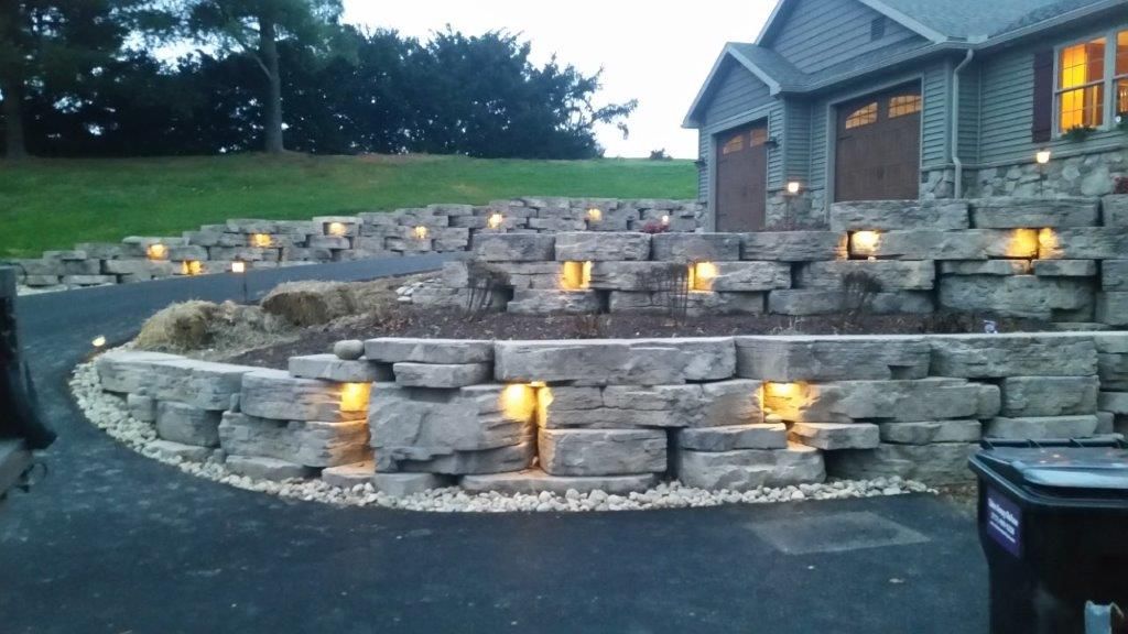 A stone wall with lights on it in front of a house