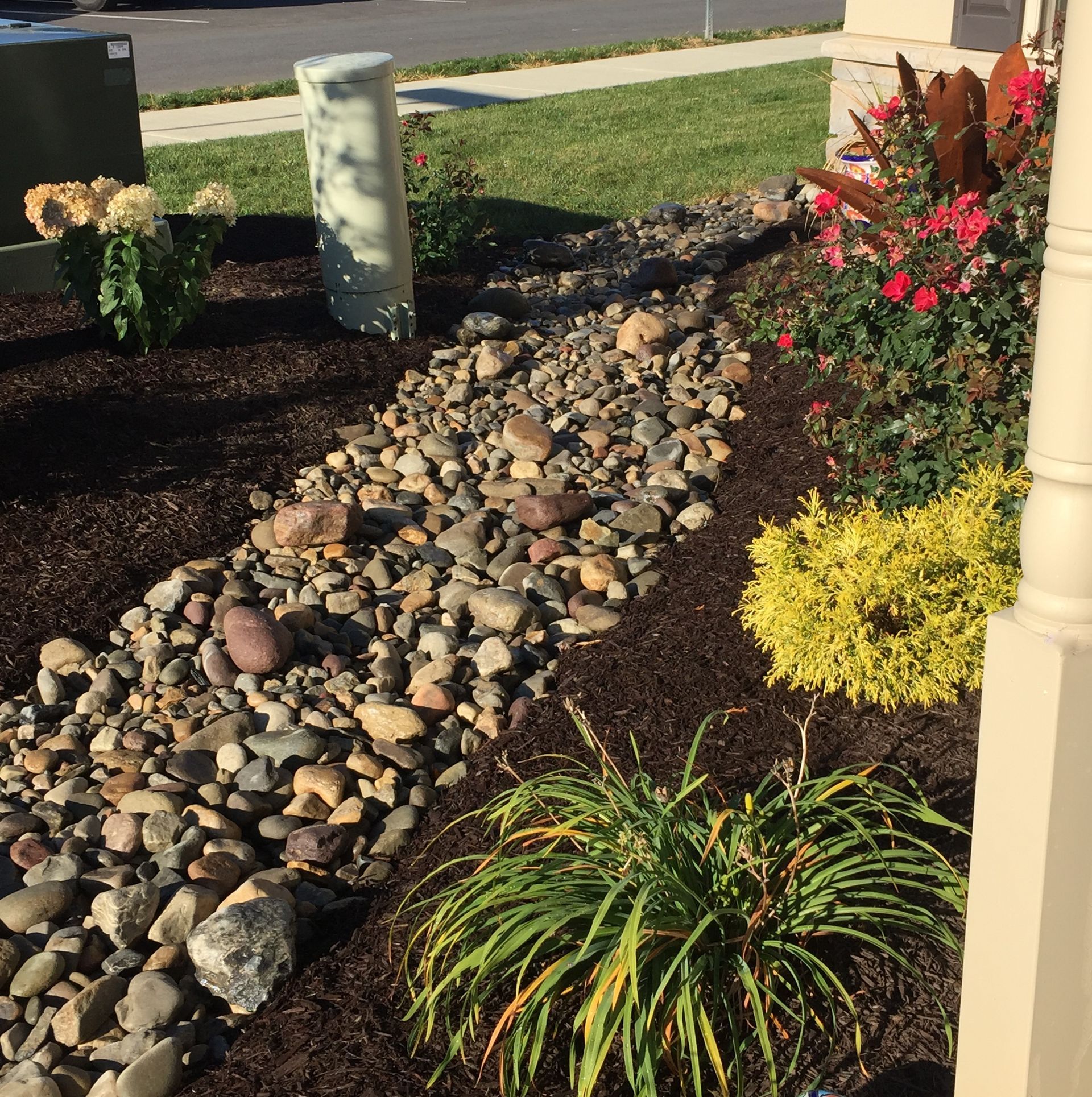 Rock garden landscaping with a stone-lined dry creek, colorful shrubs, and a front yard walkway