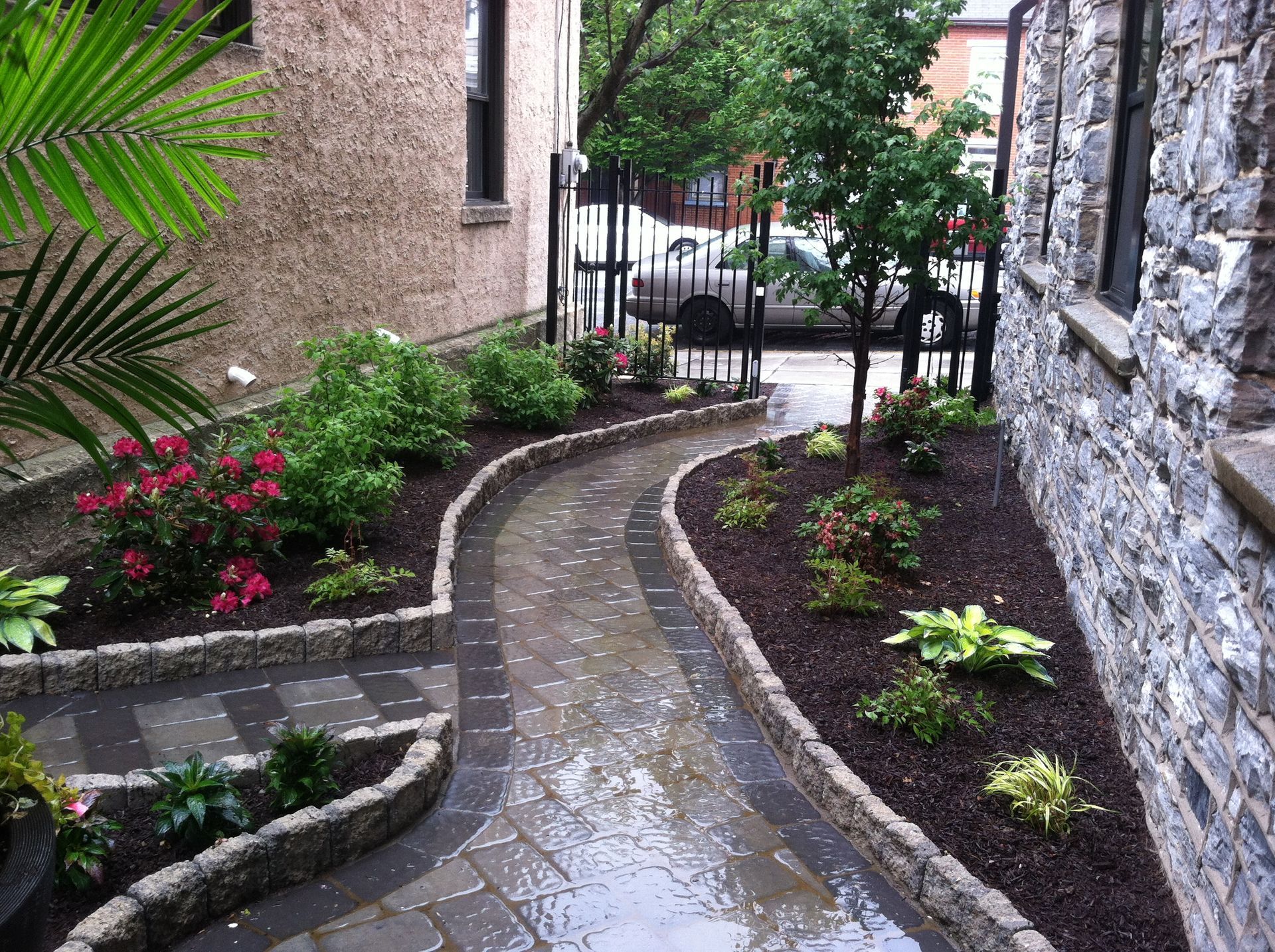 A stone walkway surrounded by plants and flowers in front of a stone building.