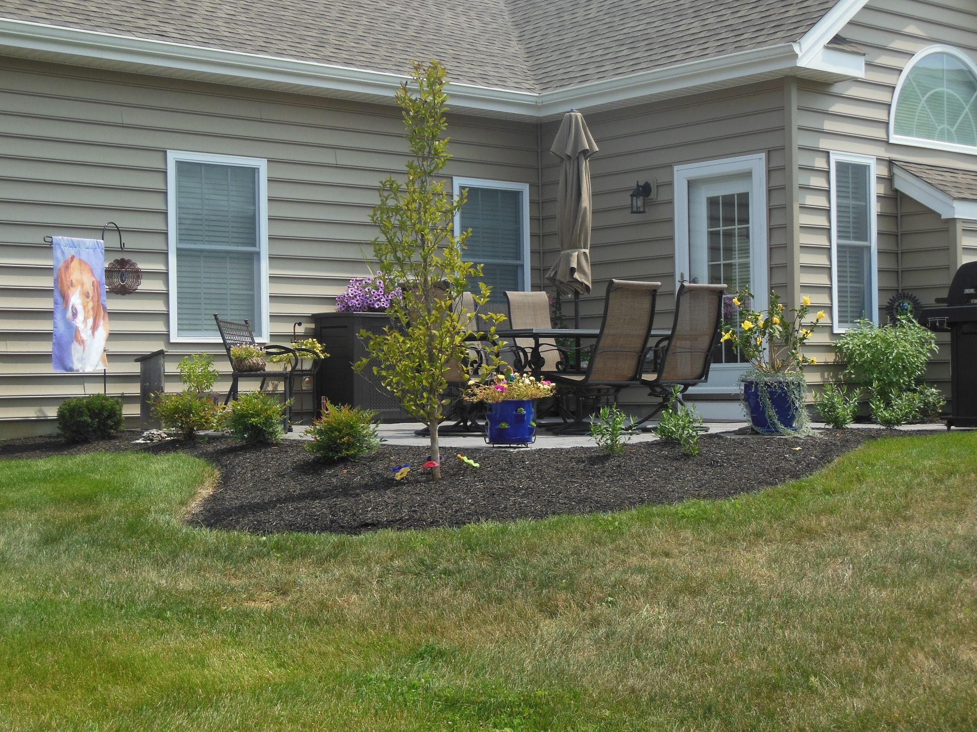 Suburban house with small landscaped front garden, patio chairs, and potted plants by the entryway.