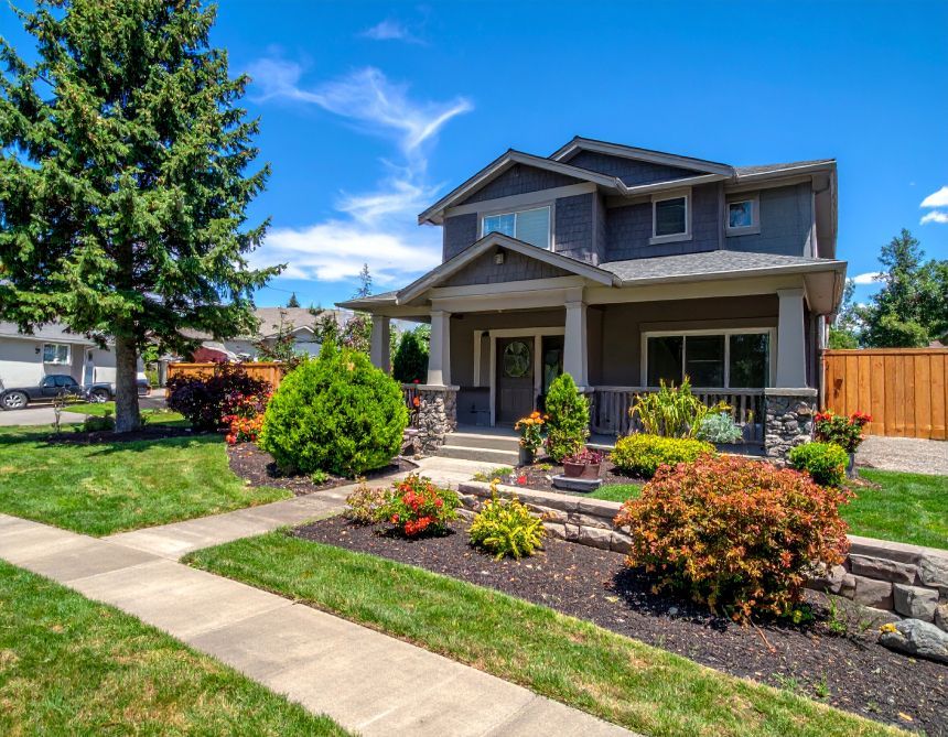 Suburban house with a front porch, landscaped yard, and a sidewalk under a bright blue sky