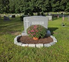 A grave in a cemetery with flowers and a cross on it.