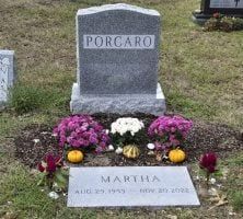 A gravestone with flowers and pumpkins in a cemetery.
