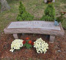 A stone bench is sitting in front of a grave in a cemetery.