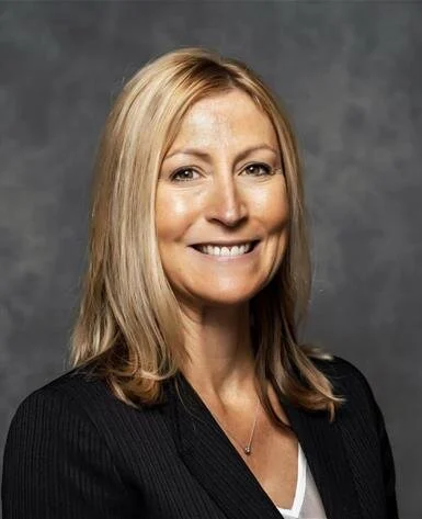 A woman in a suit and necklace is smiling for the camera.
