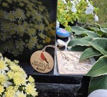 A grave with flowers and a wooden plaque with a bird on it.