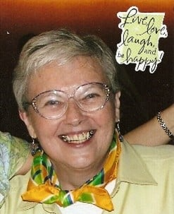 A woman wearing glasses and a scarf is smiling.