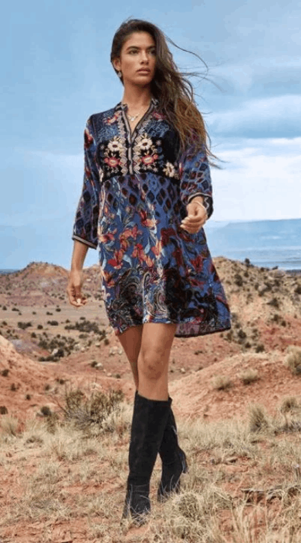A woman in a blue dress and black boots is standing in the desert.