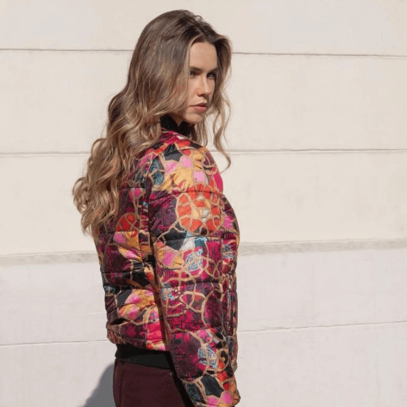 A woman wearing a colorful jacket is standing in front of a white wall