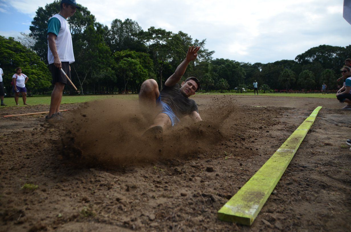 A man is doing a long jump in the dirt.