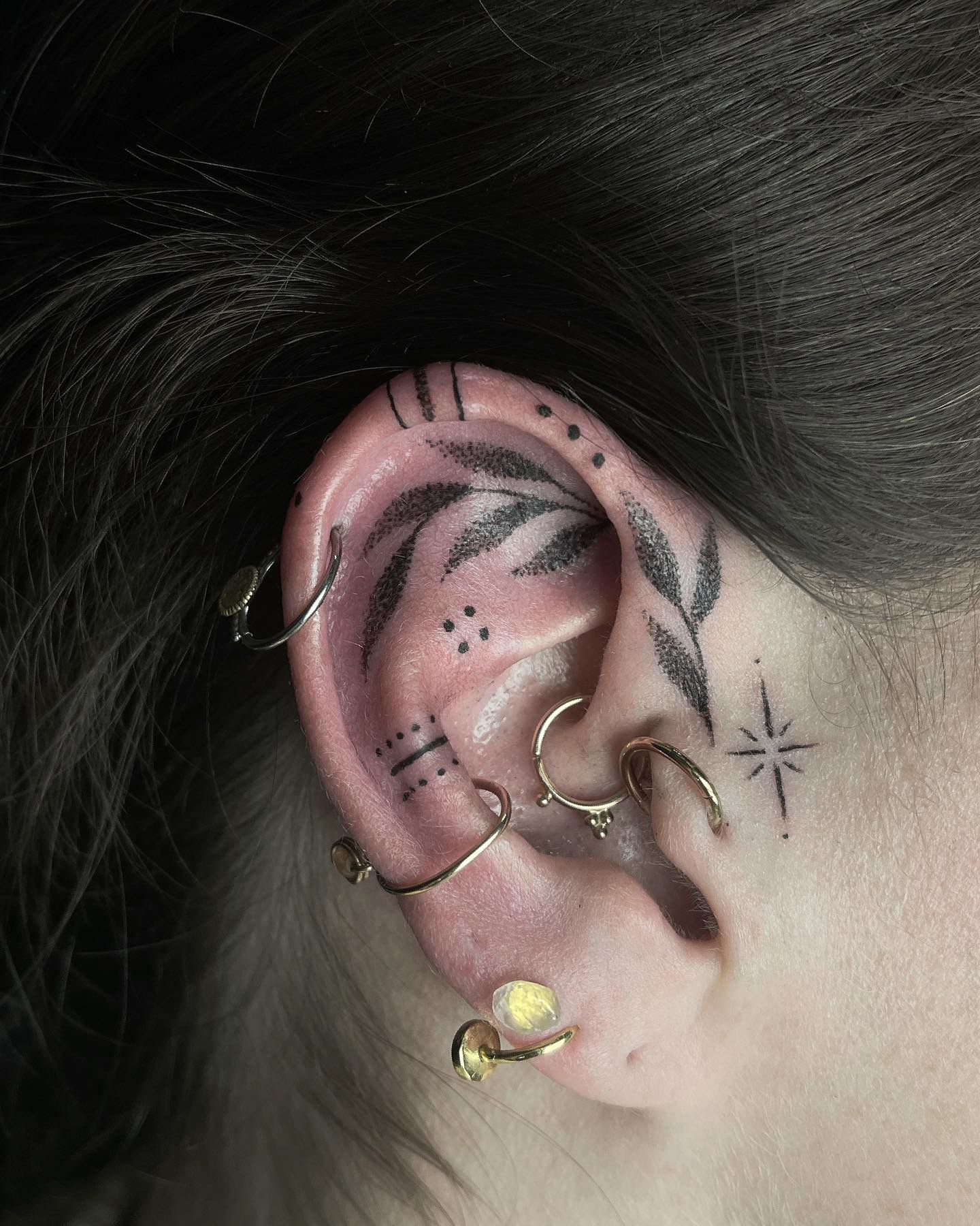 Ear with multiple gold piercings and black tattoos.