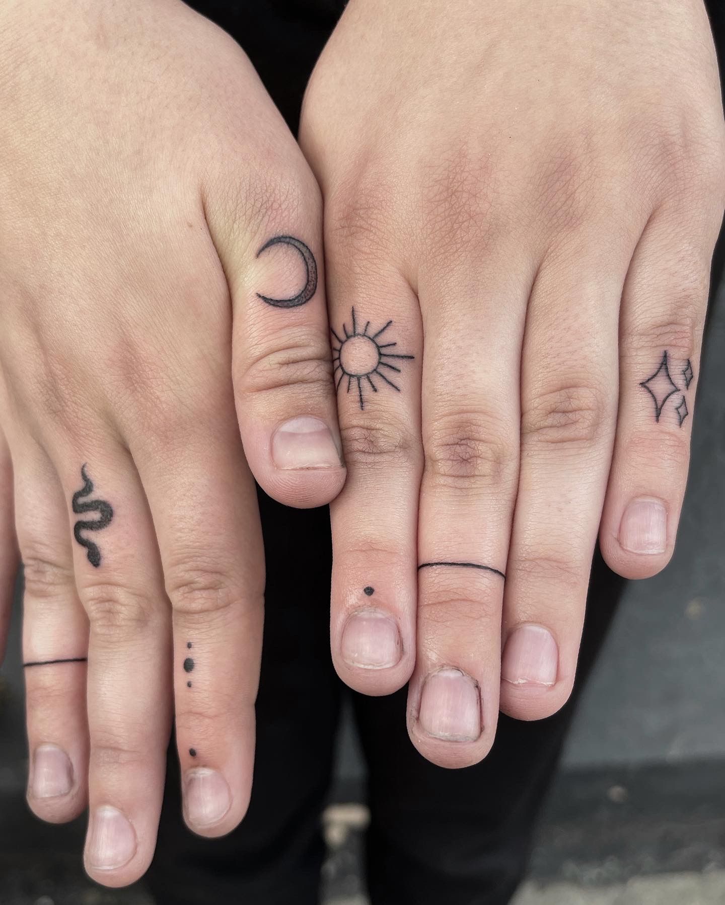 Hands with finger tattoos of a snake, line, dots, moon, sun, line, dot, and stars.