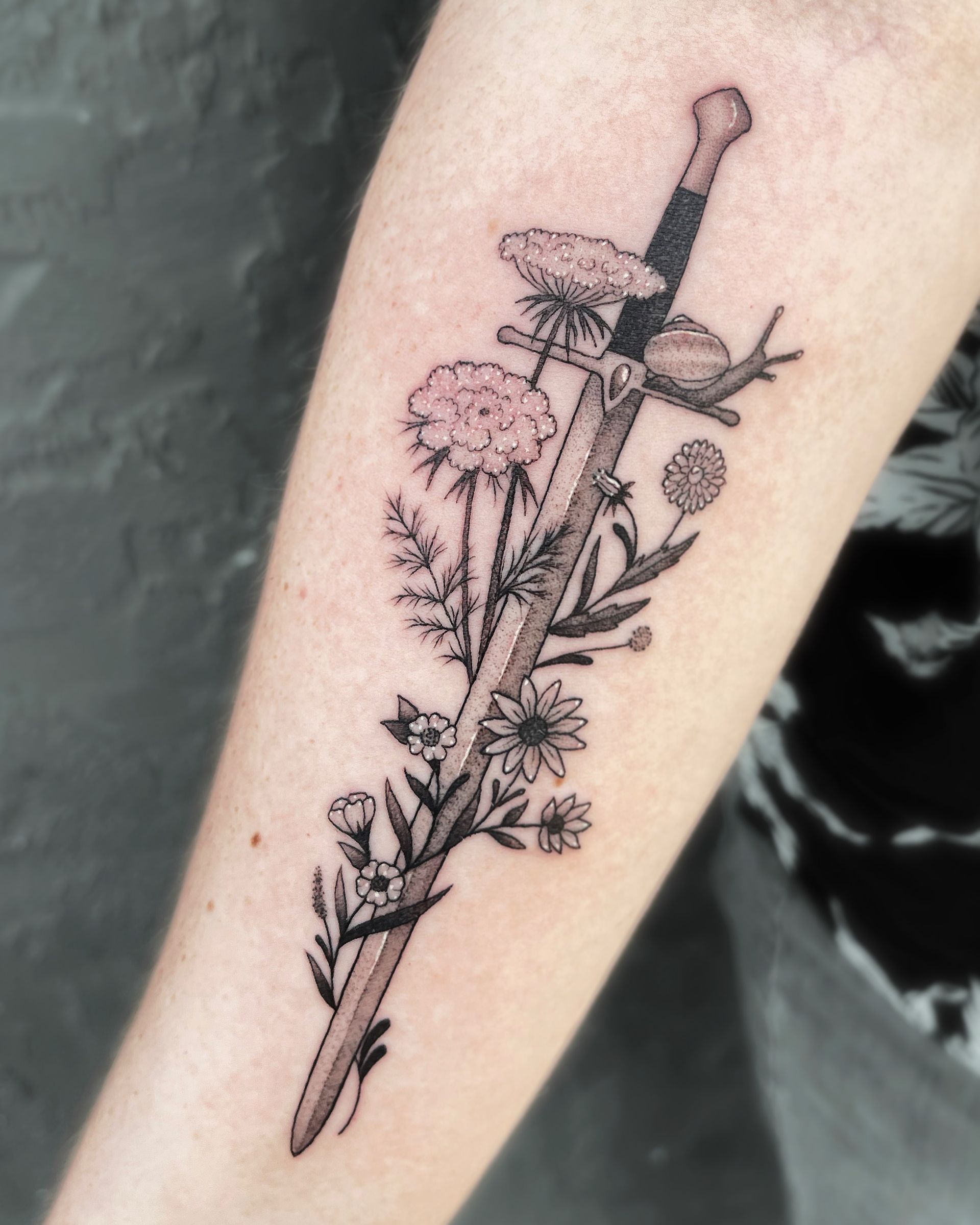 Tattoo on arm of a sword with flowers. Black and grey.