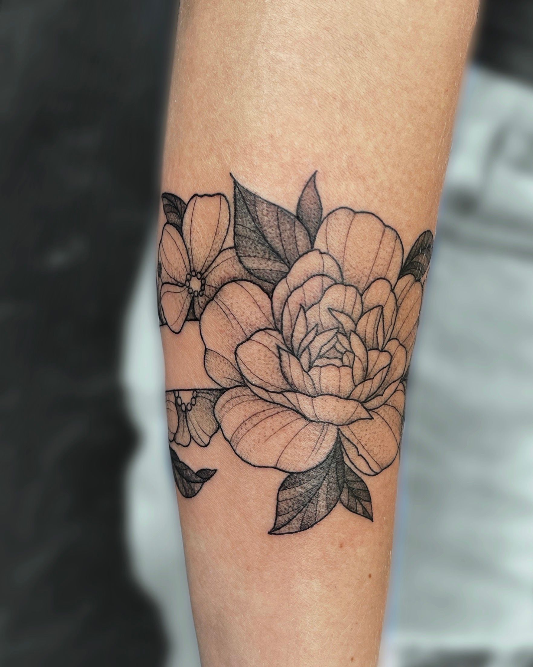 Tattoo of a peony flower with leaves on a person's arm, done in a dotwork style.