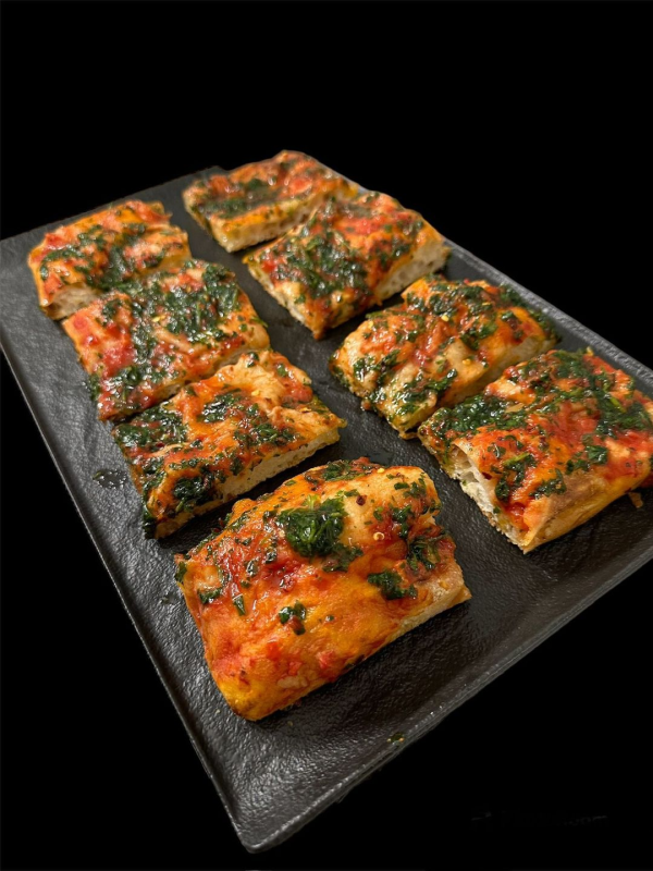 Pizza a fette con erbe aromatiche su un piatto rettangolare nero su sfondo nero
