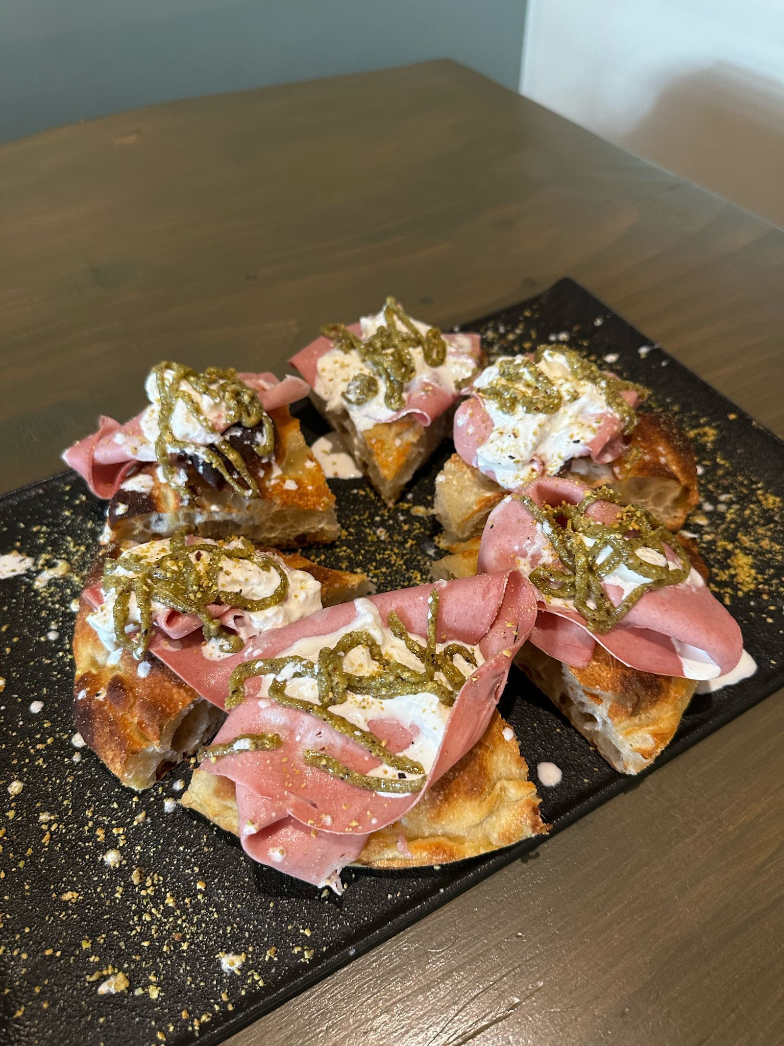 Fette di dessert guarnite con panna montata rosa, pistacchi e zucchero a velo su un vassoio nero.