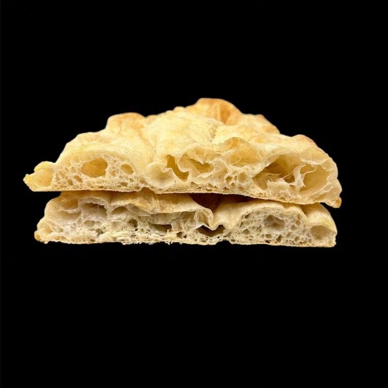 Due pezzi di focaccia soffice e dorata sovrapposti su sfondo nero.