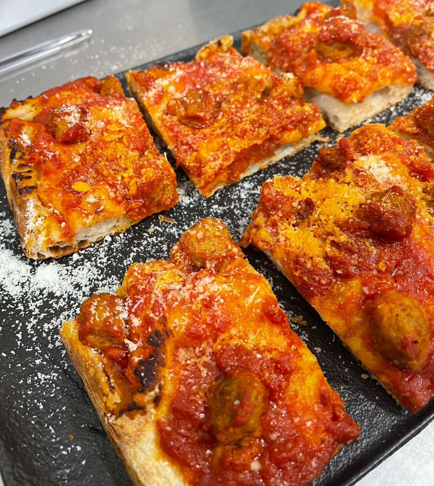 Pizza rettangolare tagliata a fette con formaggio fuso e salsa di pomodoro su una teglia scura, spolverata di farina.