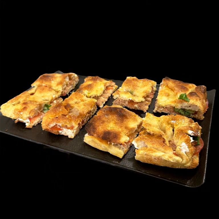 Fette di focaccia dorata a cubetti su un vassoio nero su sfondo nero