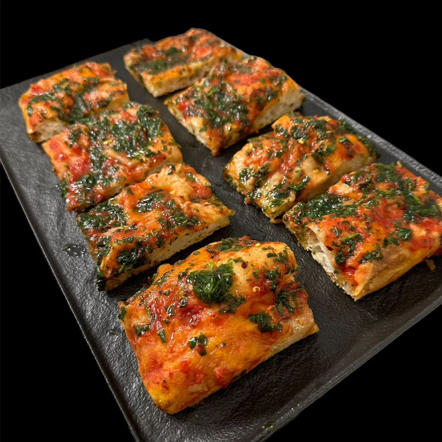 Piadina a fette con pomodoro, servita su un tagliere nero e guarnita con erbe aromatiche e formaggio.