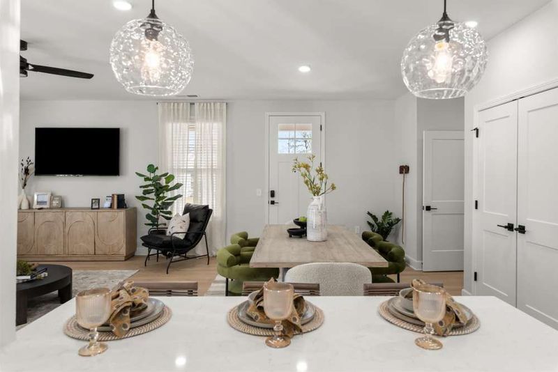 A view from a kitchen counter looking into a dining and living area featuring a wooden table, green chairs, and a TV.
