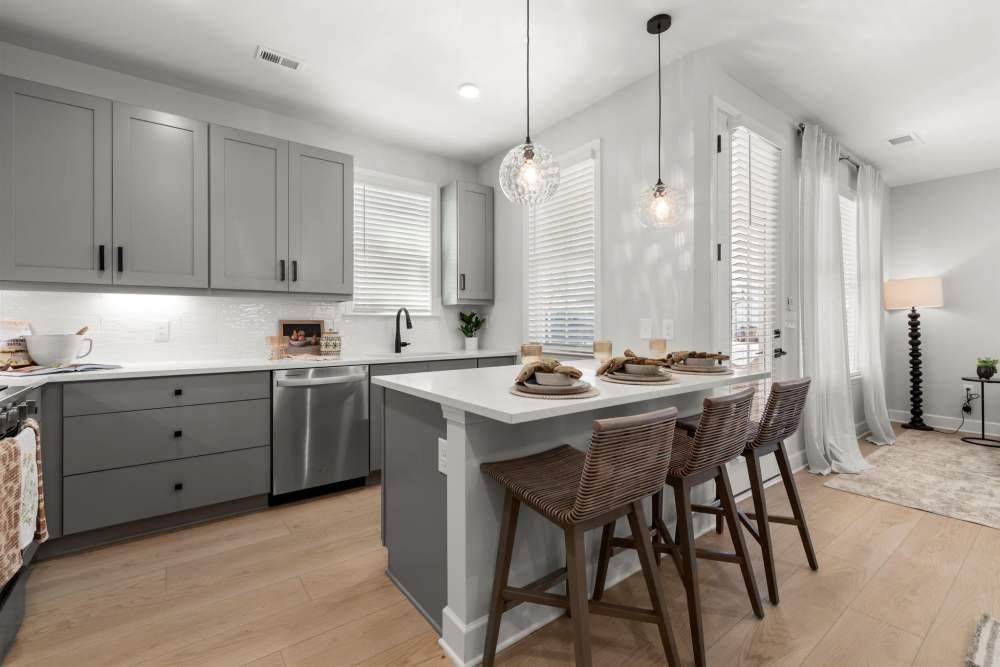Modern gray kitchen with white countertops, island with bar stools, and a doorway.