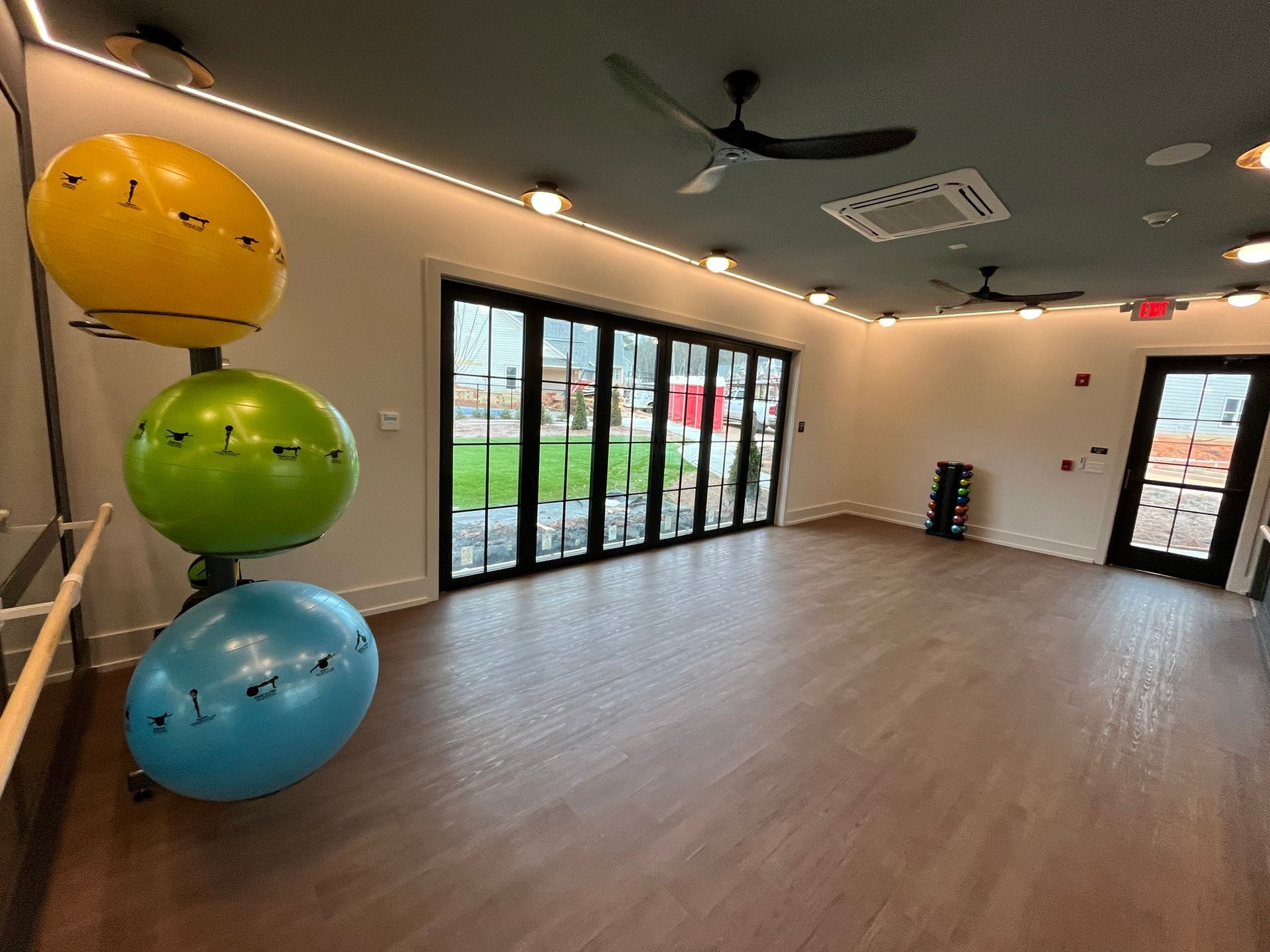 Yoga studio with colorful exercise balls, large windows, and wooden floors.