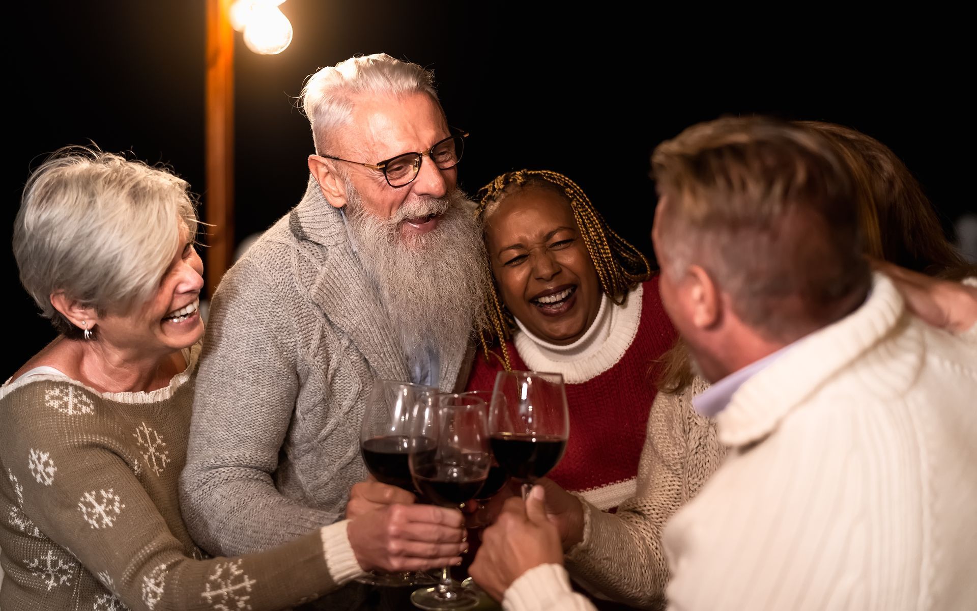 Four older men toasting beer glasses outdoors.