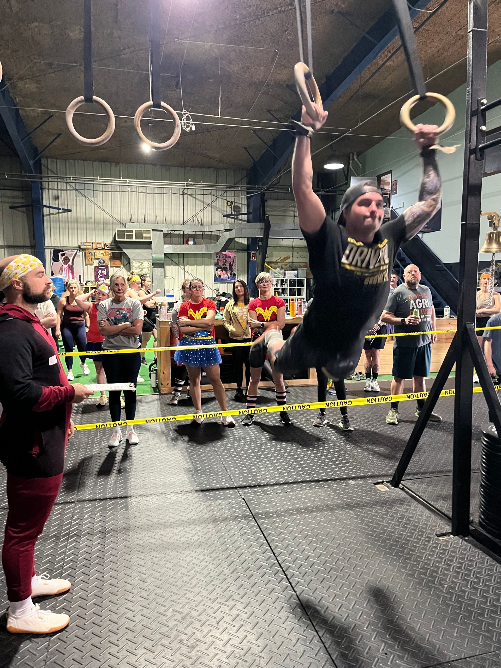 Athlete swinging on rings in an indoor obstacle course while a crowd watches behind a barrier