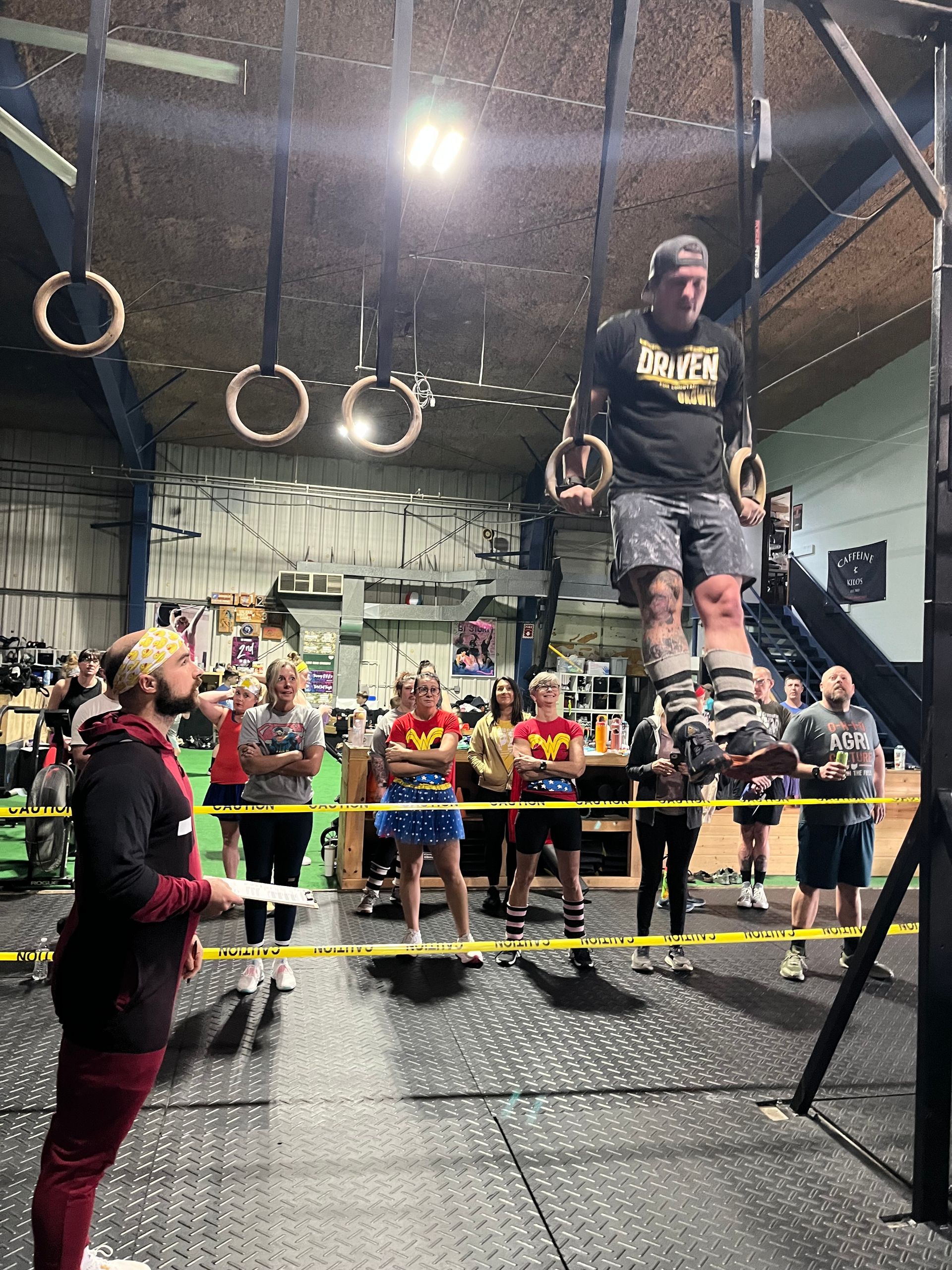 Person on gym rings above a crowd at an indoor fitness event