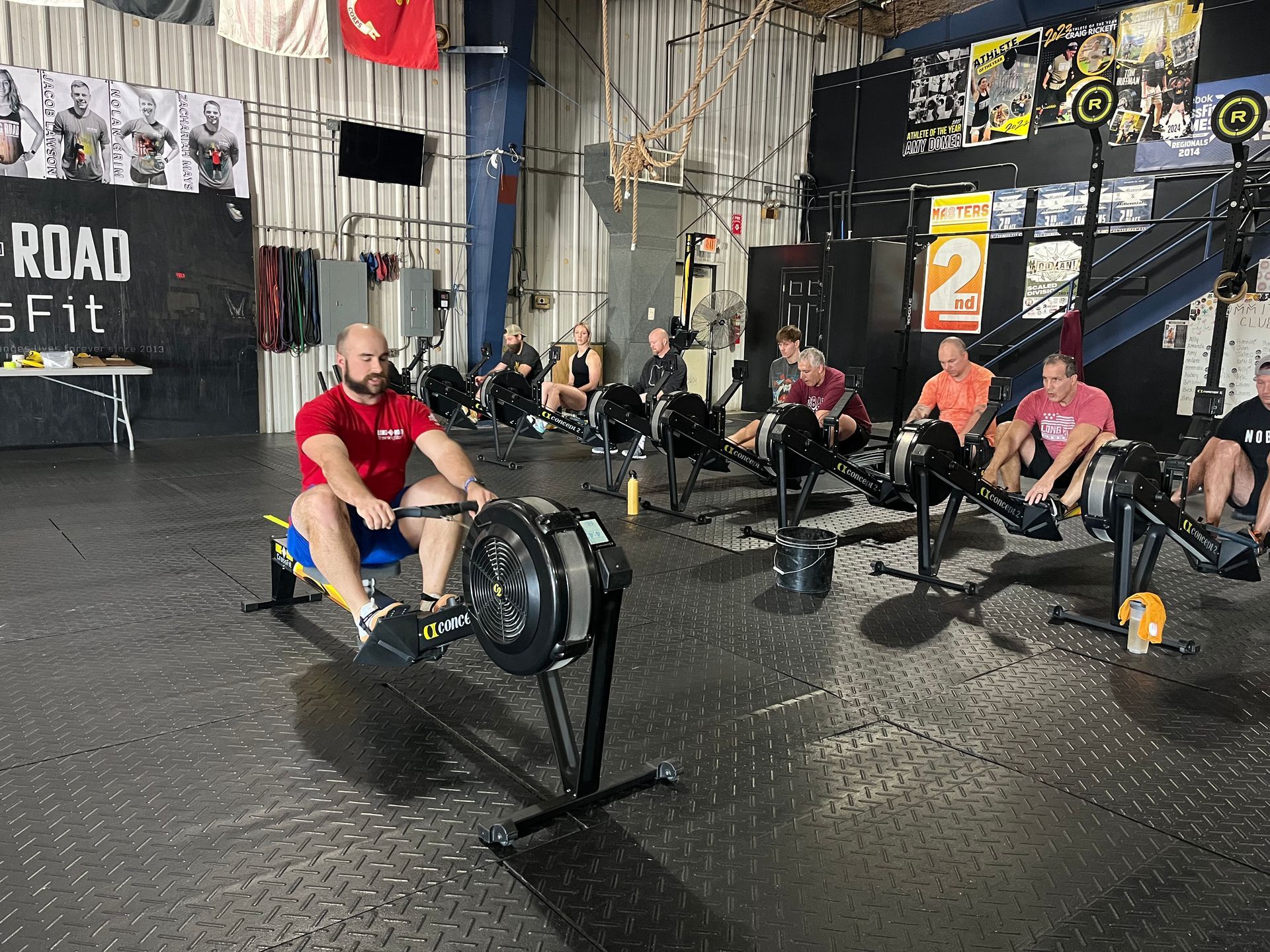Indoor rowing competition with athletes rowing on machines in a gym in Urbana, OH, spectators seated nearby.