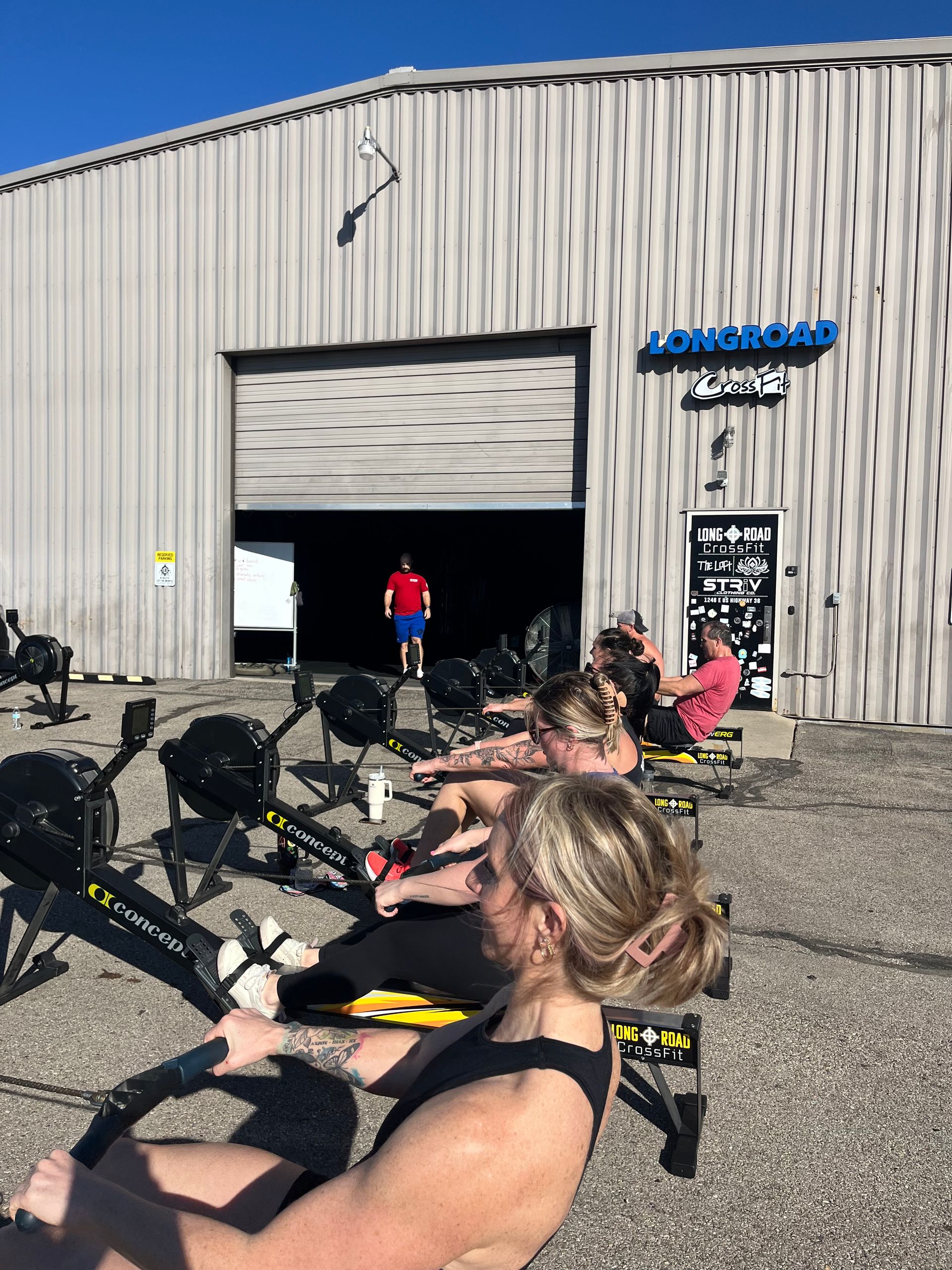 People exercising on rowing machines outside a gym with an open garage door