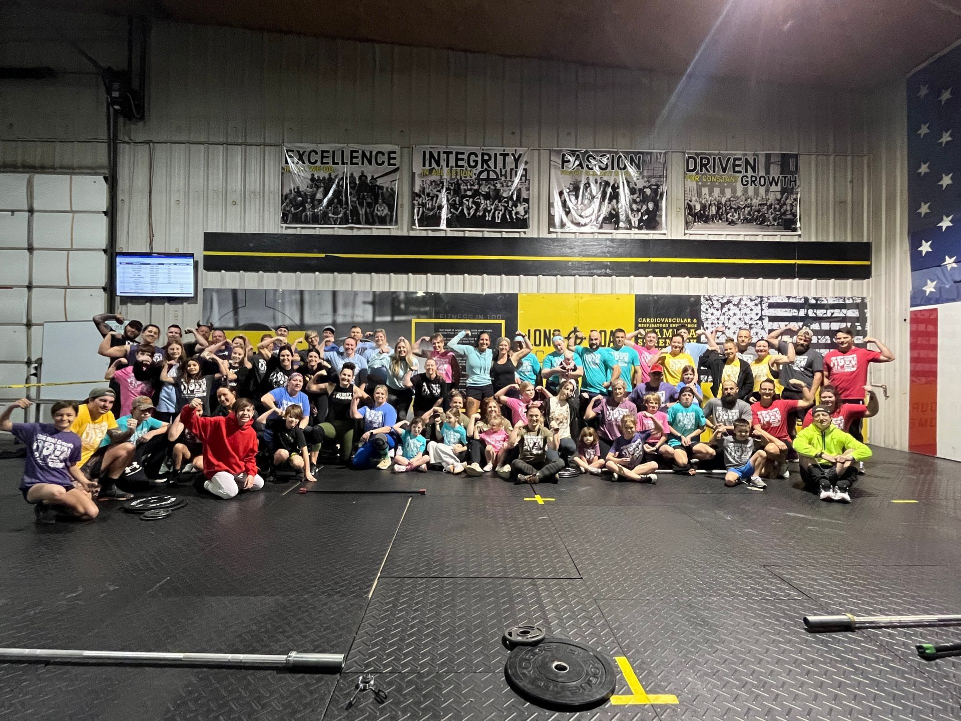 Large group posing in a gym, with colorful shirts, a black floor, and wall banners in the background.