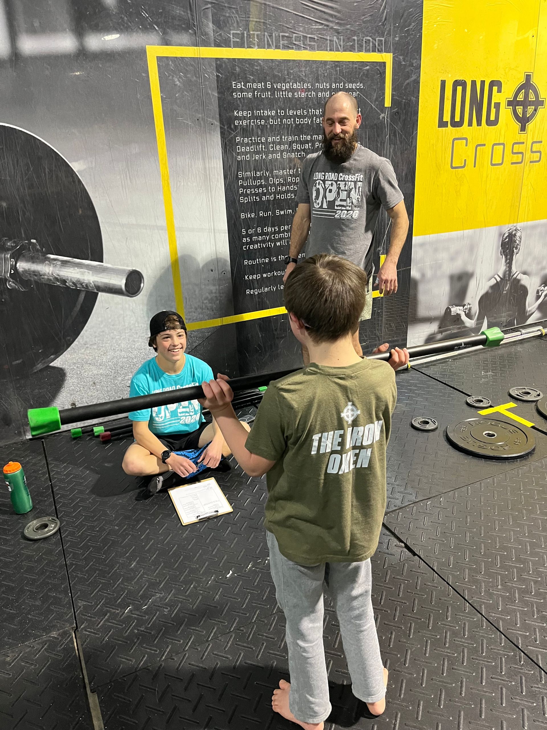 Three people in a gym, one seated on the floor, with a wall banner reading “Long Cross.”