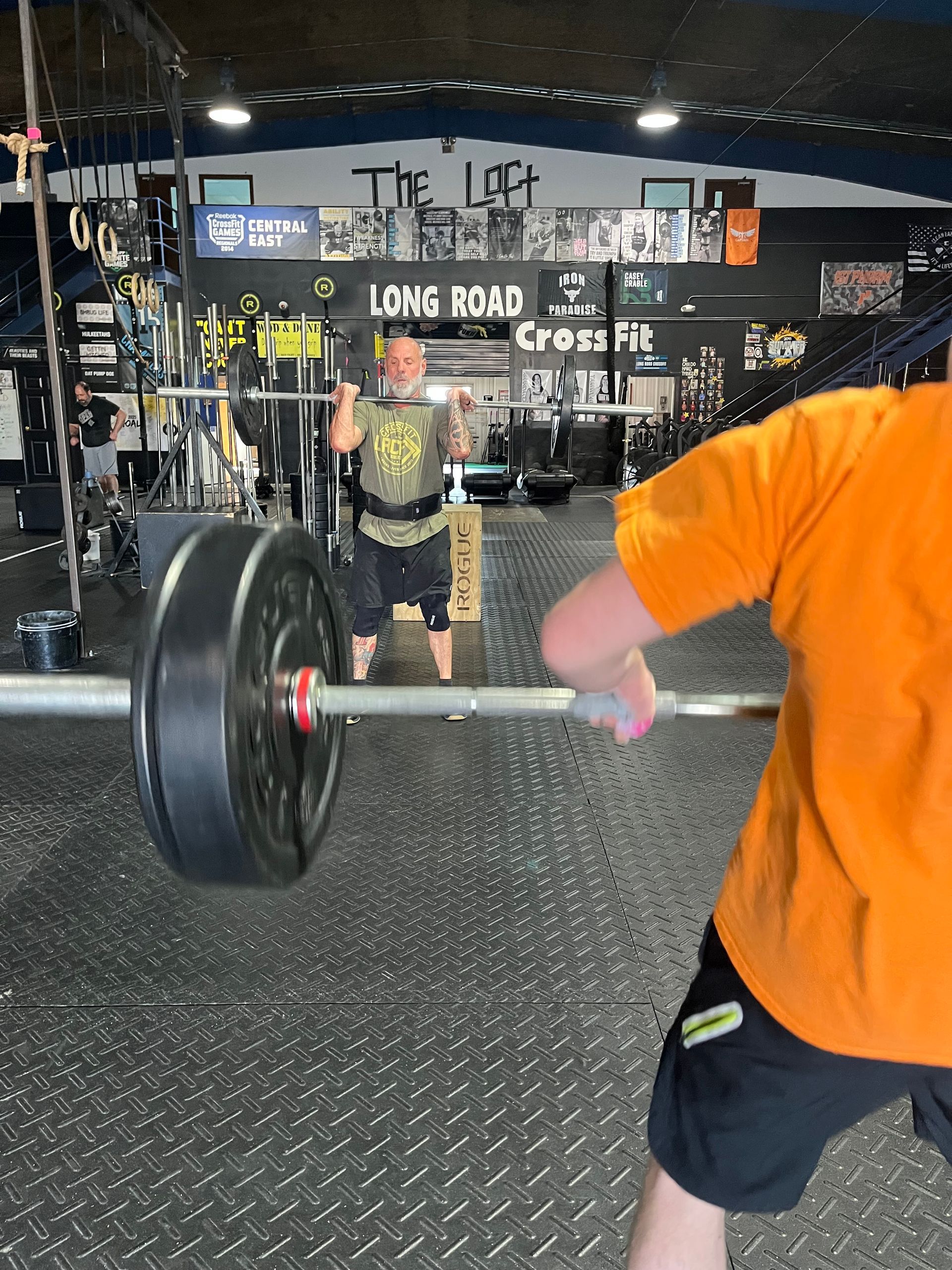 Gym scene with a person lifting a barbell in Springfield, OH, another spotting in the background.