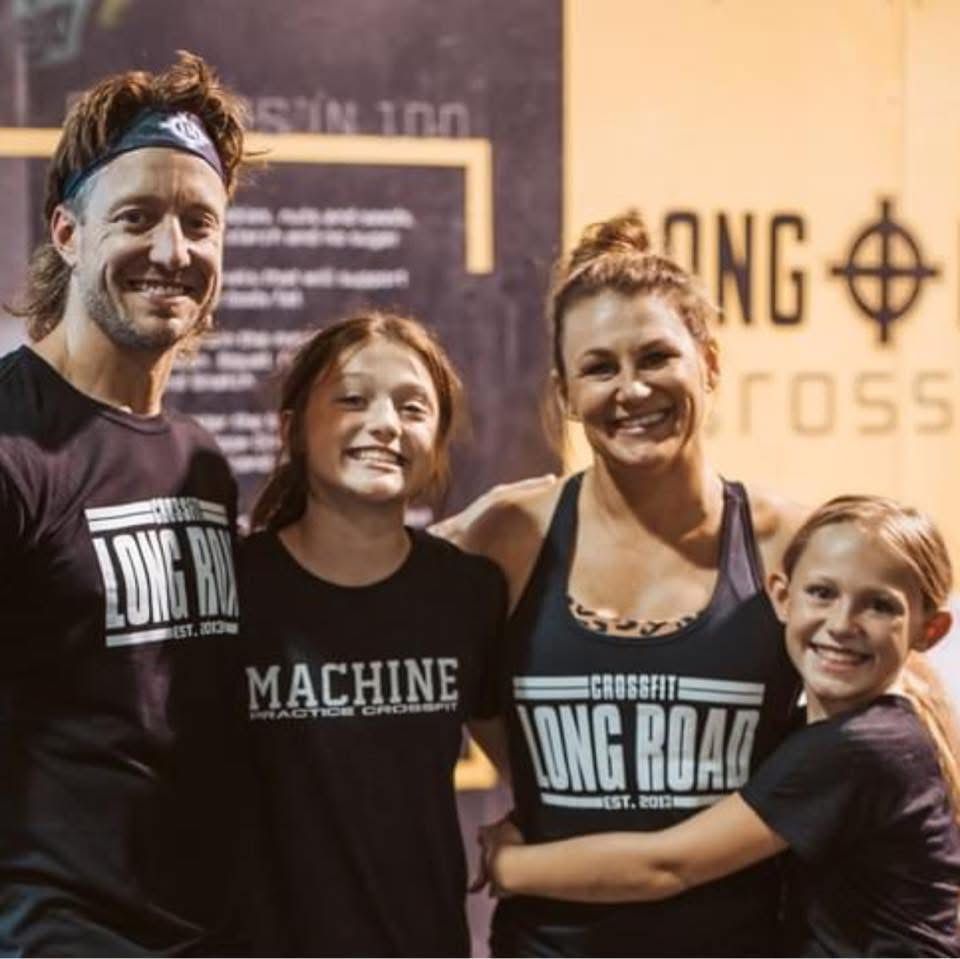Four smiling people posing at a CrossFit gym, wearing Long Road and Machine shirts