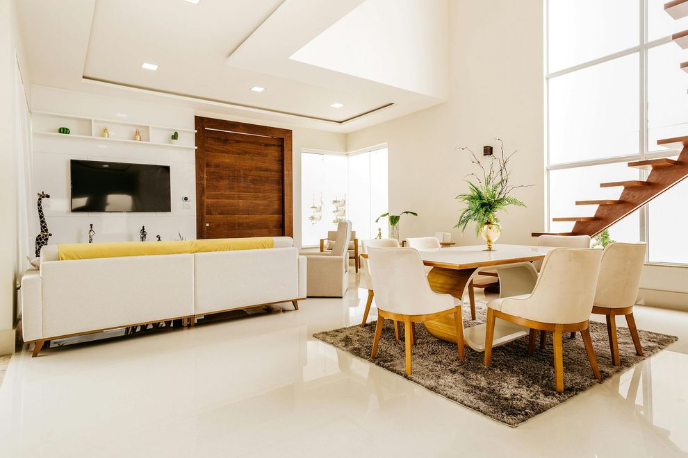 Bright modern living-dining room with white sofa, TV, round table, beige chairs, wood accents, and stairs.