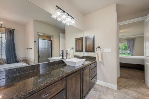 Bathroom vanity with granite countertop, double sinks, large mirror, and doorway to a bedroom with a bed visible
