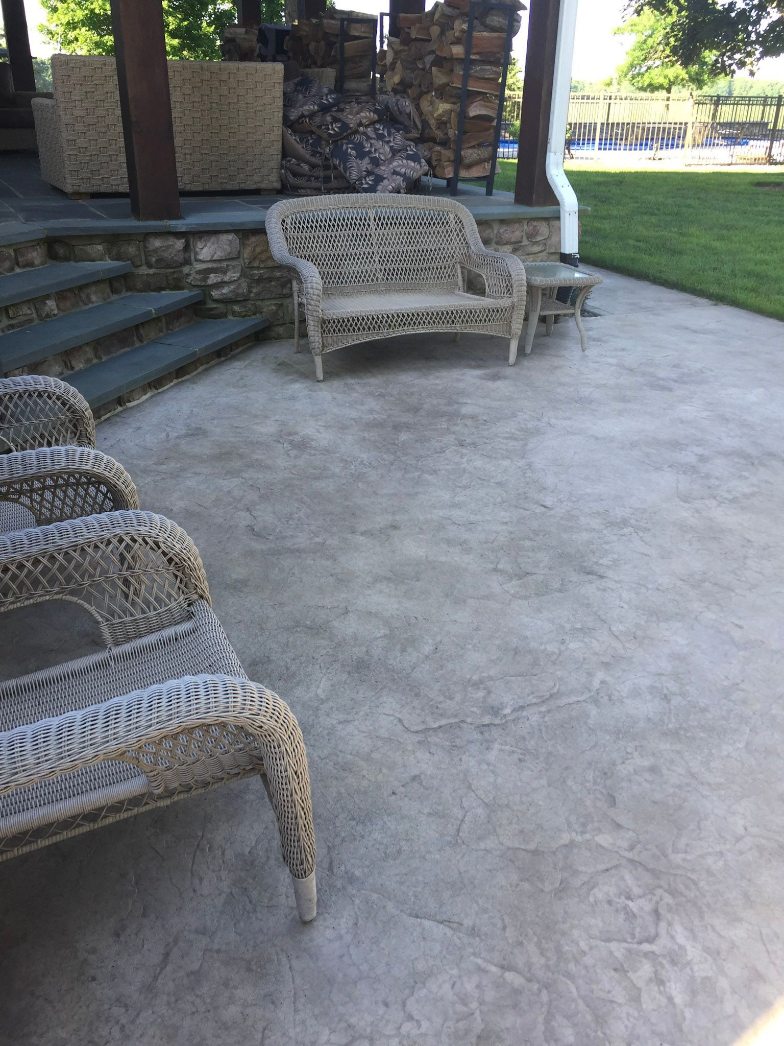 a  stamped concrete  patio with wicker furniture and a bench .