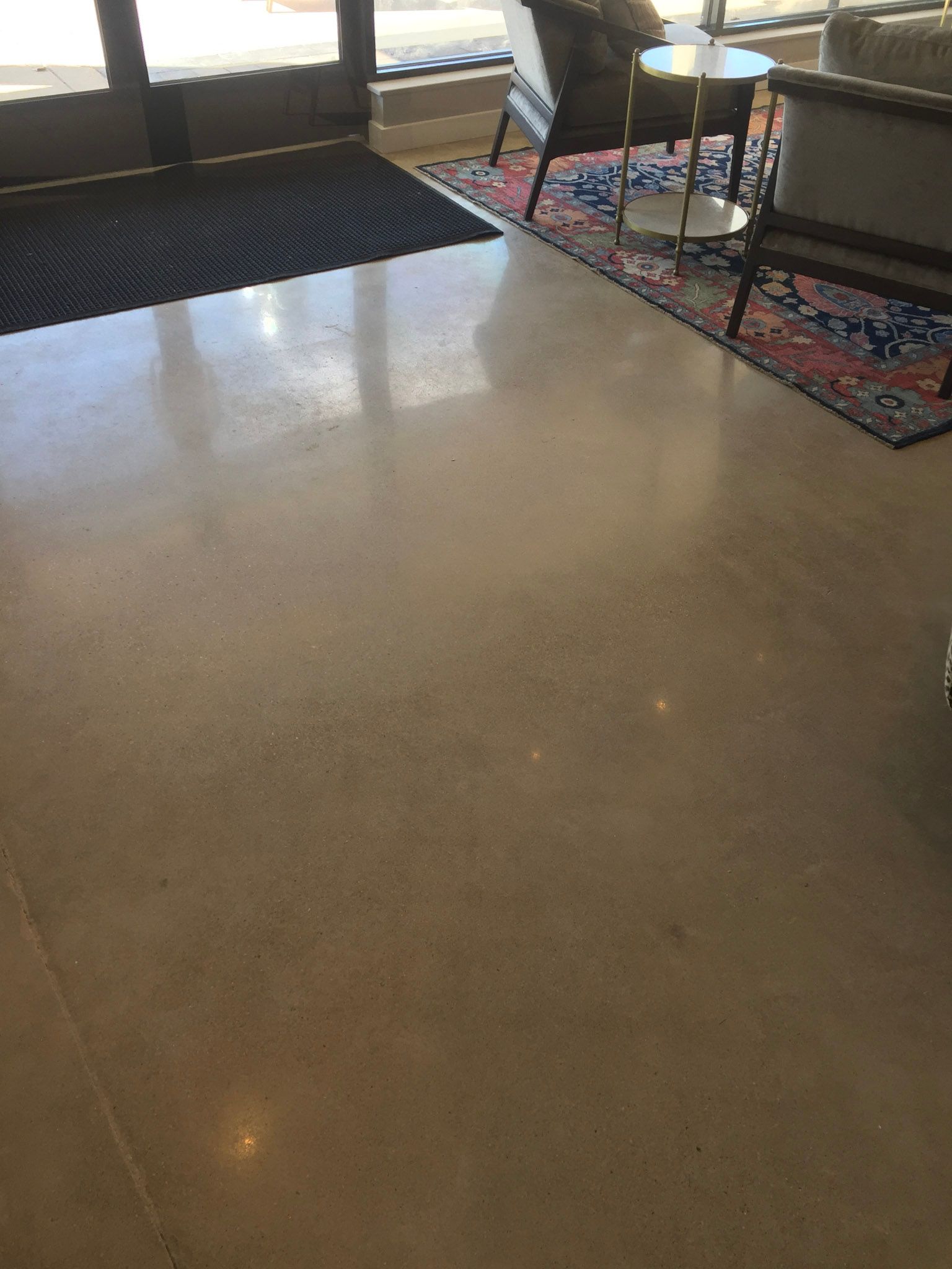 a polished concrete floor in a lobby with a couch , chairs , tables and a rug .