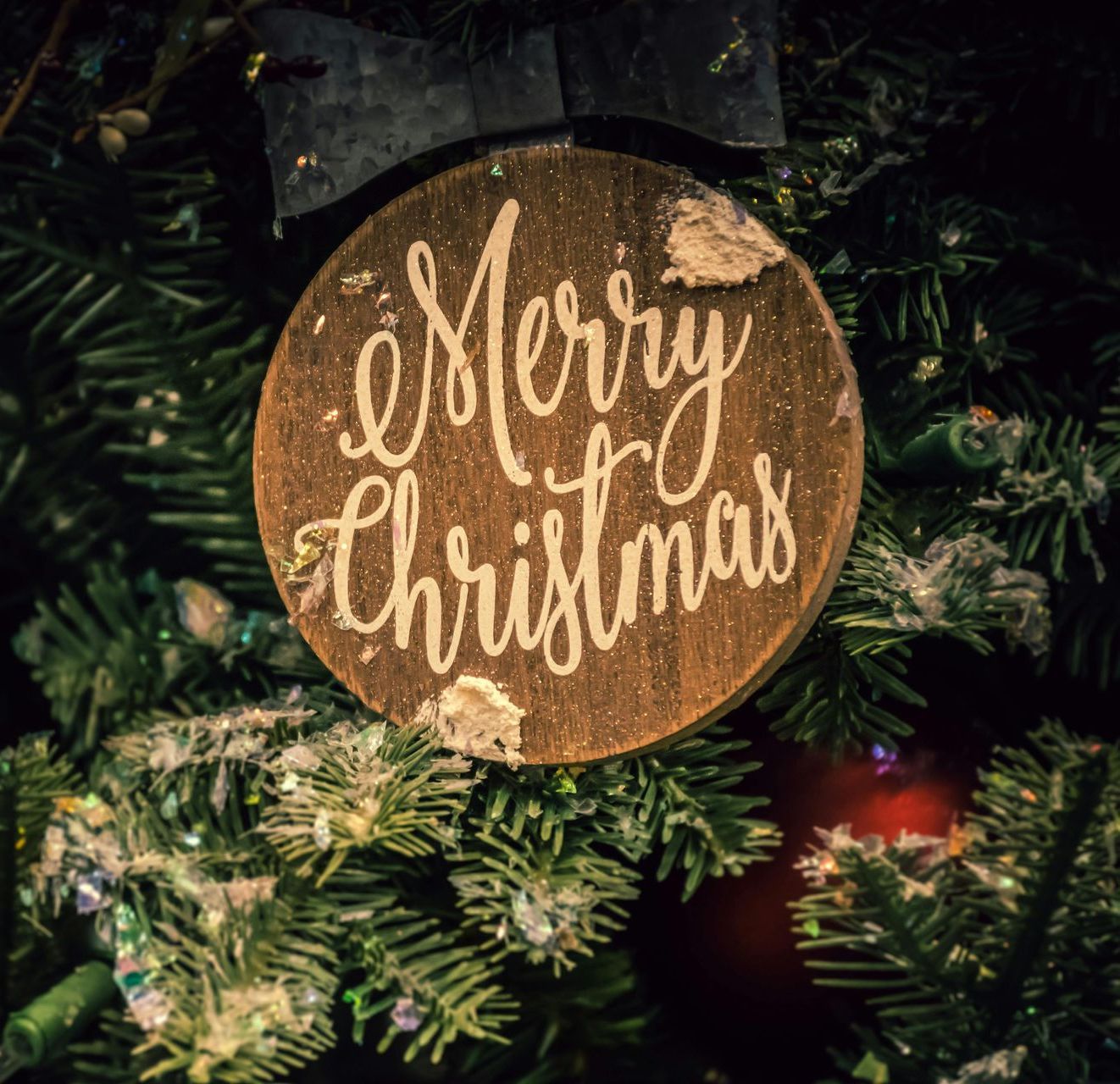 A merry christmas ornament hangs from a christmas tree