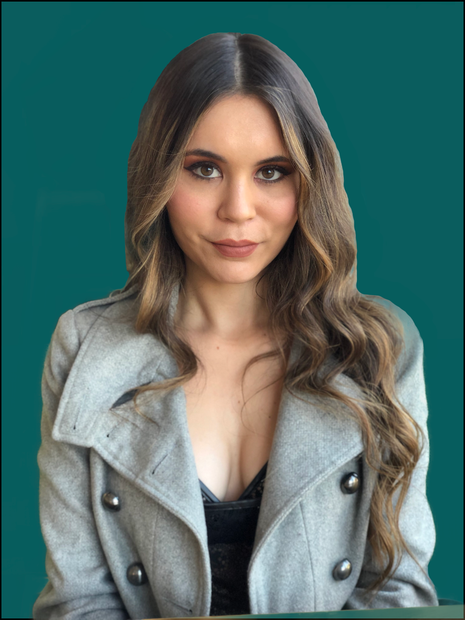 A person with long, wavy brown hair wears a light gray double-breasted coat against a solid dark teal background.