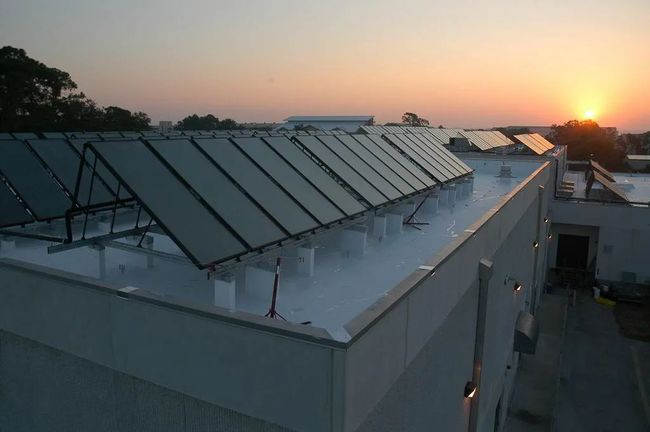 Rooftop solar panels at sunset on a white building, with trees in the background