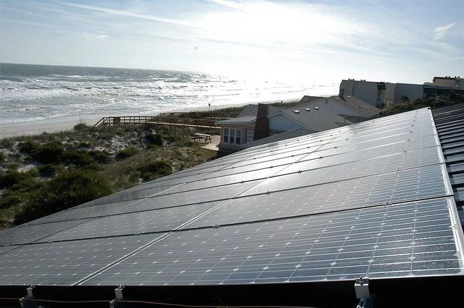 Solar panels beside a beach, reflecting bright sunlight near the shoreline