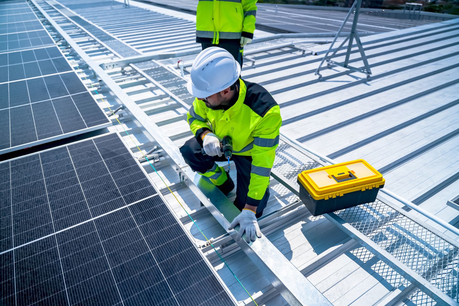 Worker in neon safety gear installing solar panels on a rooftop with tools nearby