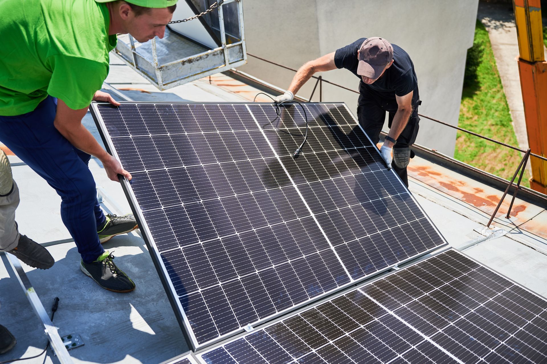 Workers installing black solar panels on a rooftop under bright sunlight