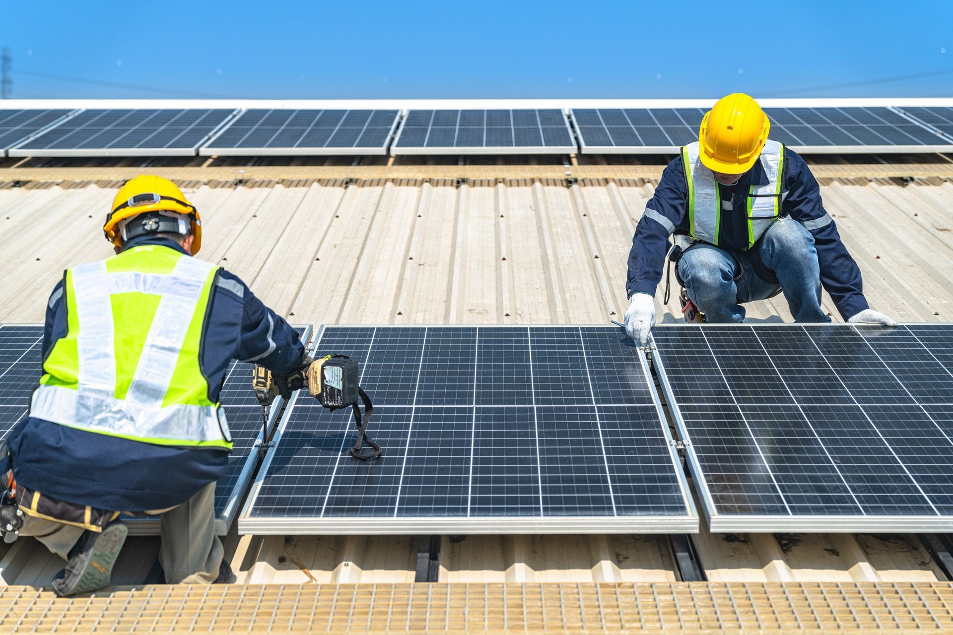 Workers installing solar panels on a rooftop under a clear blue sky