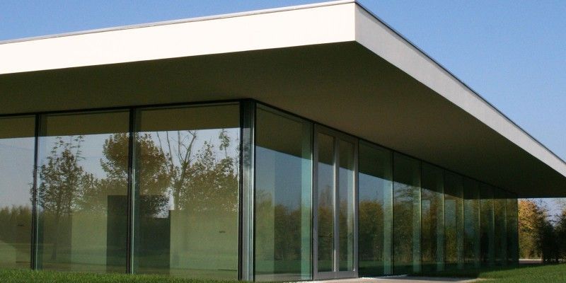 Moderno edificio per uffici in vetro con tetto bianco a sbalzo e finestre riflettenti.
