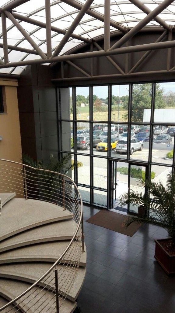 Atrio interno con scala curva, parete in vetro e vista sul parcheggio esterno.