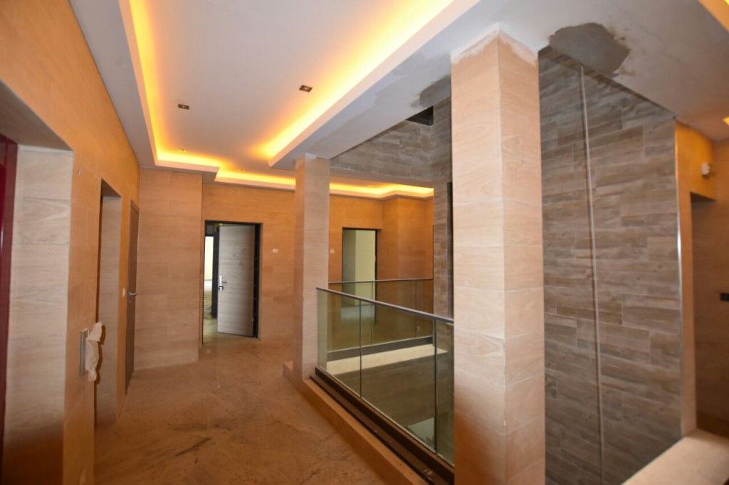 Corridoio moderno con pareti beige, faretti a incasso a soffitto e ringhiera in vetro che si affaccia su un piano inferiore.
